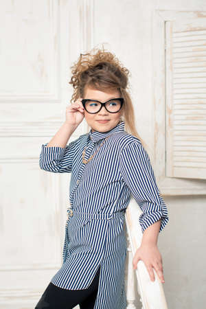 Beautiful young girl in glasses sitting on the stairs of the bright roomの写真素材