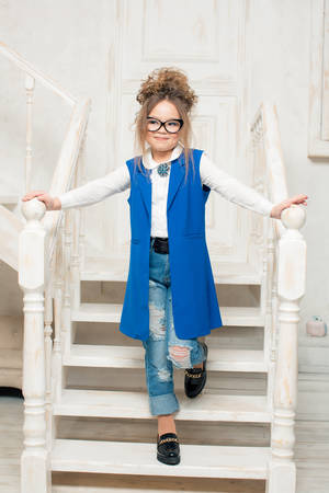 beautiful girl with glasses is standing on the stairs in the blue dress and jeansの写真素材