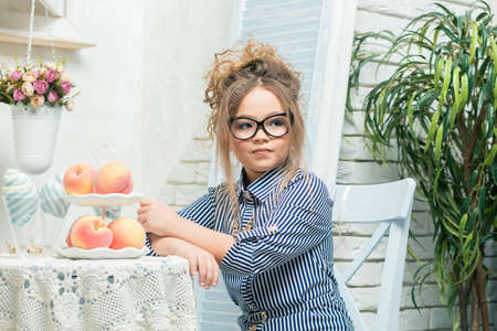 beautiful girl in glasses sits at a table with fruit in a bright roomの写真素材