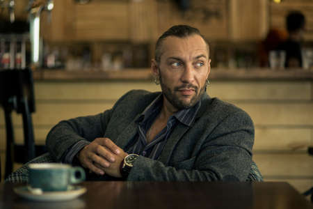 A young man with a beard, sitting in a cafe with a Cup of coffee.の写真素材