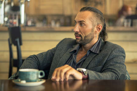 A young man with a beard, sitting in a cafe with a Cup of coffee.の写真素材