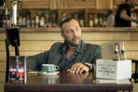 A young man with a beard, sitting in a cafe with a Cup of coffee.の写真素材