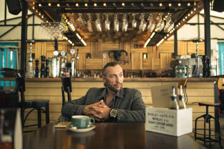 A young man with a beard, sitting in a cafe with a Cup of coffee.の写真素材