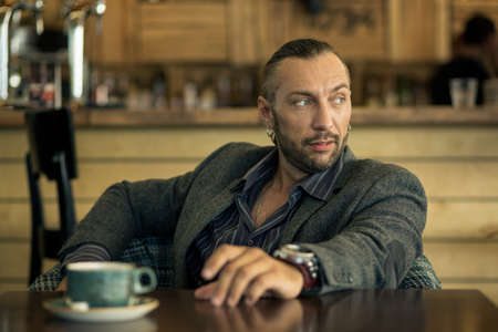 A young man with a beard, sitting in a cafe with a Cup of coffee.の写真素材