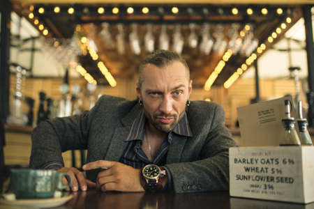 A young man with a beard, sitting in a cafe with a Cup of coffee.の写真素材