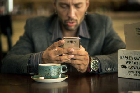 A young man with a beard, sitting in a cafe with a Cup of coffee.の写真素材