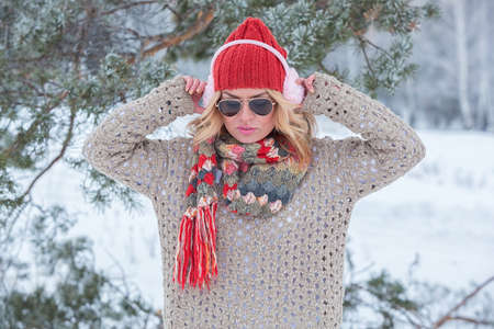 Beautiful girl in a red hat and sweater in the snow in pink with headphonesの写真素材