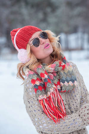 Beautiful girl in a red hat and sweater in the snow in pink with headphonesの写真素材