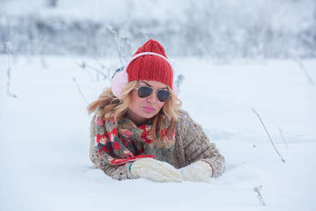 Beautiful girl in a red hat and sweater in the snow in pink with headphonesの写真素材