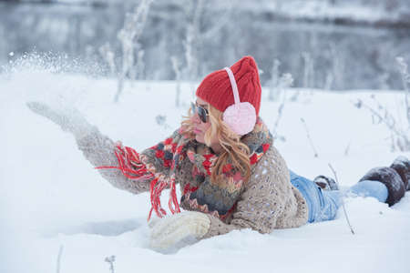Beautiful girl in a red hat and sweater in the snow in pink with headphonesの写真素材