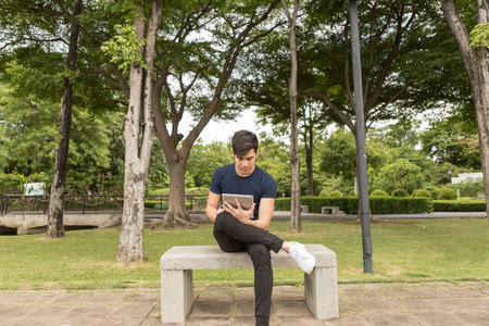 Young Business man use the tablet and sit on the chair in park.の写真素材