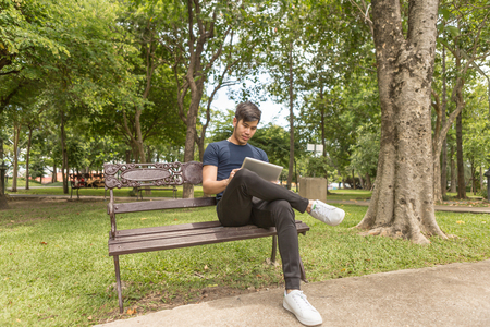 Young Business man use the tablet and sit on the chair in park.の写真素材