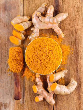 fresh turmeric roots with turmeric powder on wooden tableの写真素材