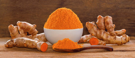 Turmeric roots with turmeric powder on wooden background