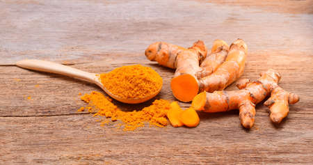 Turmeric roots with turmeric powder on wooden backgroundの写真素材