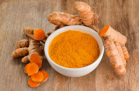 Turmeric roots with turmeric powder on wooden backgroundの写真素材