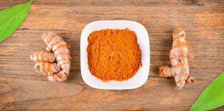 Top view of Turmeric roots with turmeric powder on wooden backgroundの写真素材