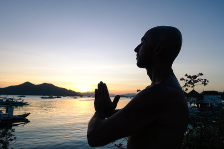 Silhouette of man doing yoga exercises at sunset on the terrace overlooking the ocean - Young person during meditation training - Concept of relaxation with twilight colors and orange filter lookの写真素材