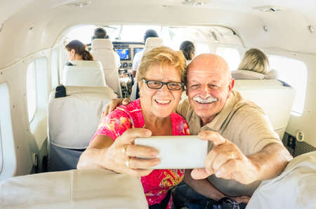 Senior happy couple taking selfie with mobile phone on board of plane  -  Smiling retired people having fun flying from Coron to Borakay by airplane - Concept of elderly happiness on world wide travelの写真素材