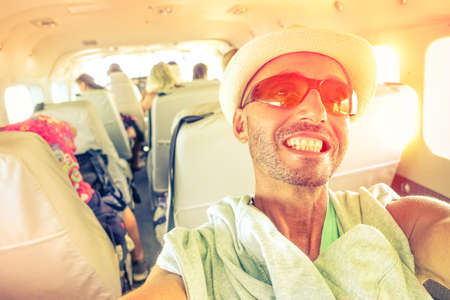 Man travel selfie inside small plane at sunset light - Cheerful tourist taking self photo with mobile phone into airplane - Concept of happiness and holidays - Vintage filter soft focus due sun haloの写真素材