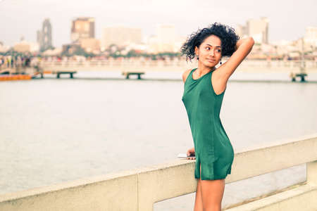Beautiful young woman at pier standing in sensual posing - Slim body latina girl holding  mobile relaxing at city sea view - Asian fashion model wearing green short dress by the river - Beauty conceptの写真素材