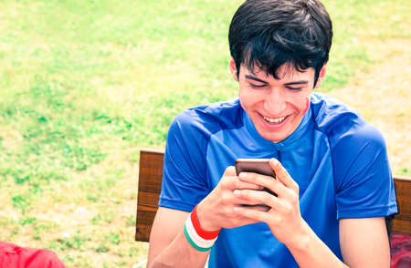 Joyful man watching mobile phone sitting on park benchの写真素材