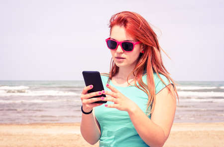 Young sad woman looking mobile phone on the beachの写真素材