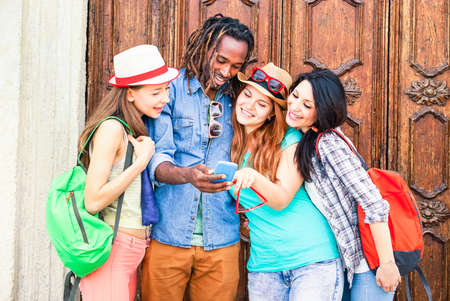 Group of multiracial friends looking mobile phone are traveling around the world - Mixed race students having fun using new smartphone technology - Concept of friendship and happiness - Focus on maleの写真素材