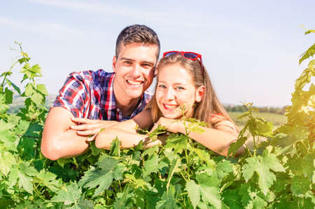 Young positive couple overlooking vine leaves in sunny summer day - Agricultural entrepreneurs leaning on grape variety smiling and looking at camera - Concept of success positivity and team workの写真素材