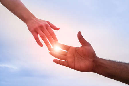 Black and white hand reaching - Handshake of different skin color hands united against racism and racial problems - Concept of human aid to migrant and refugees - Sun halo filter and dramatic lightの写真素材