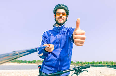 Young man with bike taking selfie outdoor by the river - Male self photo at bicycle excursion in a sunny summer day - Concept of freedom and healthy lifestyle using modern technologyの写真素材
