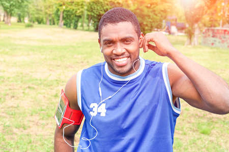 African american man jogging at city park - Black runner gay listening music with earphones while training outdoor - Concept of healthy lifestyle and sport activity with  toothy smile positive personの写真素材