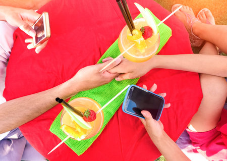 Friends hands holding phone table top view with fruit drinks - Couple using mobile scene from above...