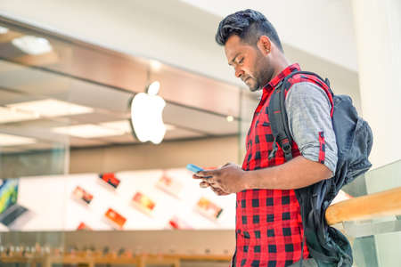 RIMINI, ITALY - JUNY 24, 2016:Man using smartphone in front of Apple store located in a shopping center on Via Caduti di Nassiriya Rimini, ITALY. Focus on mobile phoneのeditorial素材