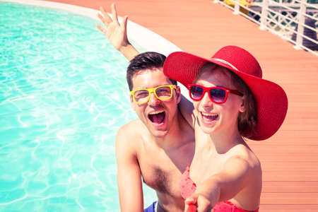 Beautiful couple having fun taking selfie at swimming pool  - Cheerful friends enjoy mobile photo camera using stick on sunny day  - Concept of happy moments on board of touristic ship - Focus on maleの写真素材