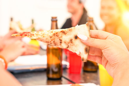 Pizza slice close up view at friends sunset party - Young people having fun eating and drinking outdoor - Concept of teenage joy and happy moment shared together at summer vacations -の写真素材