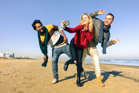 Multiracial group of friends having fun dancing on the beach while taking selfie - Young funny...