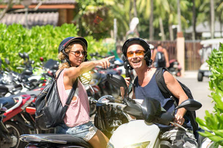 Happy couple sitting on scooters pointing during city tour - Young woman and smiling man riding motorcycle - Travel the island with wheelers is a funny vacation - Concept of joy and freedom on wheelsの写真素材