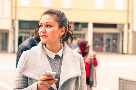Young woman thinking face with mobile phone is standing on the street -  Portrait of thoughtful girl...