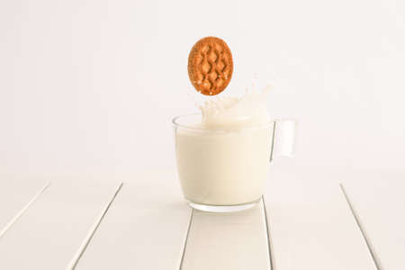 Cup of milk splashing with cookie falling inside - Glass on white table and bright background for copy spaceの写真素材
