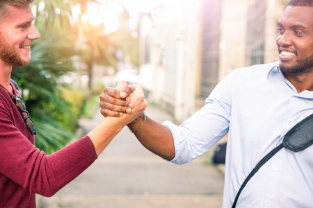 Interracial friends greating each other with handshaking in the street cropped image - Young...