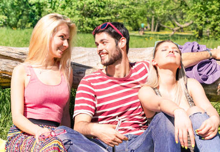 Best friends suntanning on sunny summer day at city park - Teenagers looking each other with joyful eyes sitting next to old tree trunk outdoor - Concept of teenage summer love and youth relationshipの写真素材