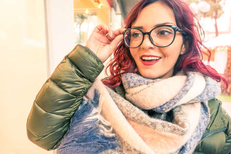 Young woman holding eyeglasses with happy facial expression walking in the street - Portrait of cheerful hipster girl with positive attitude standing outdoor at winter  - Concept of carefree lifestyleの写真素材