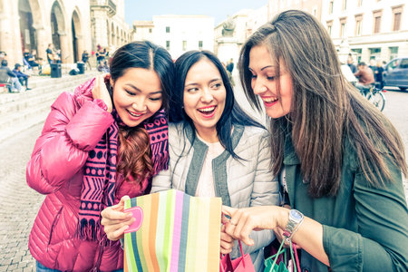Cheerful girlfriends looking inside shoppìng bag - Group of young women on winter holiday standing at city central square smiling and showing gifts - Concept of leisure and friendshipの写真素材