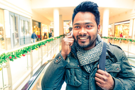 Young happy indian man making phone call smiling and wearing winter clothes - Handsome asian student using mobile having cheerful attitude - Concept of communication and successful lifestyleの写真素材
