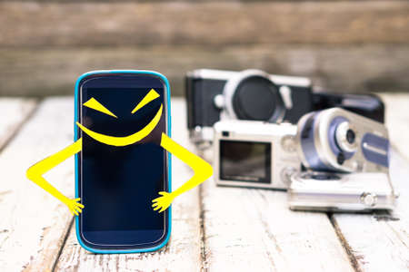 New mobile smart phone superhero with funny expression of pride standing on wood with old cameras background - Telephone vs entry level cameras - Marketing and sales  concept of photography devicesの写真素材
