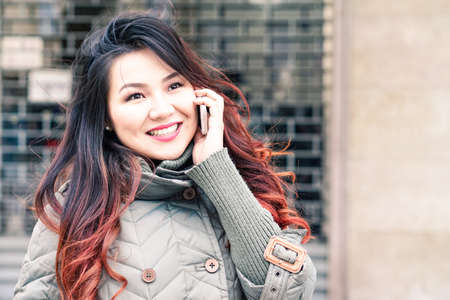 Beautiful asian woman using mobile and smiling outdoors at winter time - Happy young lady making phone call with positive facial expression - Lifestyle concept and modern technology with copy spaceの写真素材