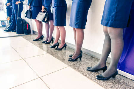 Row of stewardess and pilot at departure gate ready for boarding wearing blue airline uniform - Flight crew standing aligned by international airport - Perspective of attendants legs  focus on middleの写真素材