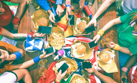 Barbeque supporters party around table holding phone - Top view of fast food lunch table with people using mobile as modern lifestyle and technology addiction concept - Vintage nostalgic filter lookの写真素材