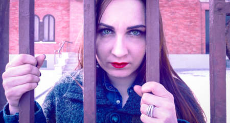 Sad woman behind bars staring intently into the eyes of camera with depressed  facial expression hopeless - Concept of people mental heath and  today social human problems - Vintage magenta filterの写真素材
